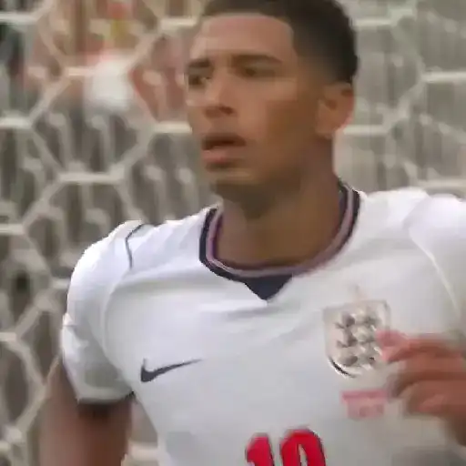 Jude Bellingham celebrando un gol con el puño cerrado y gesto de alegría. Fondo de red de portería y césped.