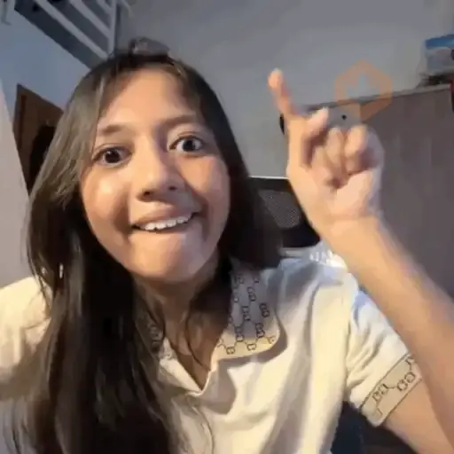 Chica joven sonriente con cabello oscuro largo, levantando el dedo índice como señalando o teniendo una idea, fondo interior de habitación